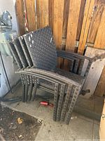 Six stacked outdoor lawn chairs made of dark brown synthetic rattan wicker weave.