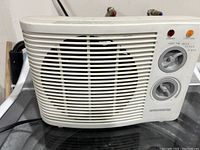 Front side view of white small heater showing slatted fan cover, two rotary control dials, red and orange indicator lights on top right corner, and Wonderheat branding.