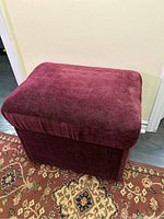Photo of the small red velvet bench from an angle showing its cushion and fabric texture.
