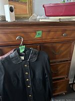 Close-up of chest of drawers with a black leather-trimmed jacket hanging in the foreground, showing drawer fronts and metallic knobs.