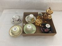 Photo showing the full tea set arranged in a box on a white surface, including gold-plated pot, sugar bowl, creamer, and four assorted porcelain cups and saucers.