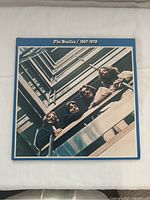 Front cover of The Beatles 1967-1970 vinyl album showing the band looking down a stairwell with blue border.