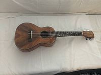 Front view of KOYAMA ukulele showing rich wood grain, sound hole, four strings, and bridge.