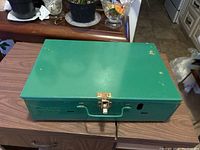 Closed green metal Coleman camping stove with latch and handle visible