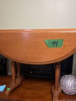 Front view of the vintage drop leaf solid wood end side table showing the rounded drop leaf top and turned legs attached to a stretcher base.