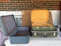 Three vintage luggage cases of different sizes. Blue case open showing gray interior, green case open showing yellow lining, black case closed.