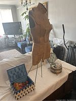 Vintage dress form mannequin next to rectangular woven sewing basket with sewing supplies on table