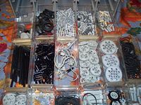 Top-down photo of compartmentalized trays holding assorted new LEGO Technic parts including gears, rods, connectors, and tires in white, black, gray, and tan colors.