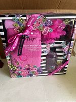 Front view of Betsey Johnson deluxe bath set in box showing wrapped pink shower wrap, shower puff, and body wash bottle in floral packaging with branded pink ribbon.