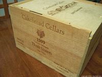 Close-up of the side of the wooden wine box showing Cakebread Cellars 1999 Three Sisters branding and vineyards illustration.