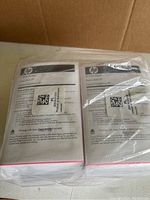Two thick stacks of HP photo paper sealed in clear plastic packaging, showing packaging labels and white paper sheets.