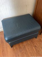 Front top angle view of the large blue leather ottoman showing the cushion and leather texture.