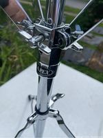 Close-up of Mapex logo on clamp mechanism, showing chrome finish and adjustment knobs on drum stand.