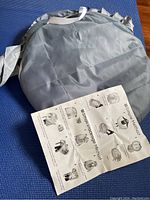 Folded gray mosquito net screen alongside instruction sheet showing folding methods and storage techniques.