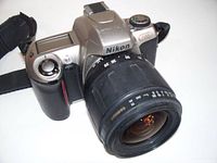 Front right angle view of Nikon N65 35mm film SLR camera showing silver body, black grip, shutter button and lens mount with Tamron 28-80mm lens attached.