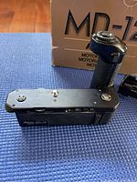 Photo showing the Nikon MD-12 motor drive with textured grip, control buttons, and original box behind it.