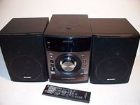 Photo of Sharp mini stereo system with central unit, two speakers, and remote control in front on white background.
