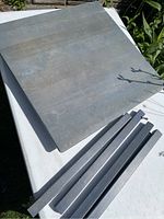 Photo showing the square blue table top with visible surface texture and four detached legs laid out beside it.