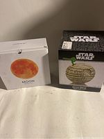 Photo showing two boxed items: one Star Wars Geekitiki apple-shaped Death Star collectible and one Moon Light box with orange moon image.