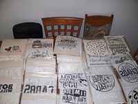 Photo showing multiple T-sheet transfer sheets with different designs arranged on a table with two wooden chairs in background.