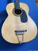 Top body of vintage acoustic guitar showing wear, strings, black pickguard, bridge, and tailpiece.