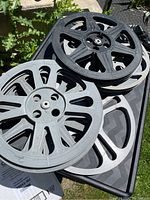 Top view of nine assorted vintage film reels in black and gray metal construction stacked together outdoors.