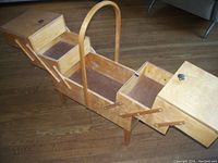 Photo showing the vintage sewing cabinet fully expanded with multiple tiers of drawers and compartments open, highlighting the cantilever folding design with a central carrying handle.
