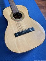 Full view of guitar body showing natural wood finish, nylon strings, and decorative sound hole rosette.