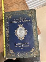 Cover of the Illustrated London News Coronation Record Number 1937 booklet, showing navy blue leather-like binding with gold decorative elements and title.