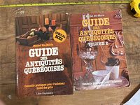 Photo showing two hardcover books titled 'Guide des Antiquités Québécoises' by Michel Ste-Marie, placed side by side on a wooden surface with measuring tape for scale.
