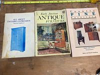 Photo displaying three antique furniture price guide books side by side on a wooden surface with a measuring tape showing approximately 20 inches.