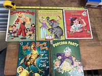 Top view of all five antique children's story books with measuring tape showing size.