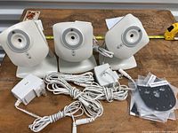 Three ADT wireless cameras on stands with power cords and adapters laid out on a wood surface