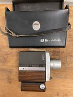 Bell & Howell vintage Focus-Matic movie camera resting on wooden surface next to carrying case with strap