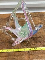 Triangular carnival glass art glass bowl showing pink, green, and blue iridescent colors with measuring tape showing length about 9 inches.