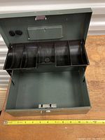 Open cashbox showing internal dividers and compartments with tape measure for size reference
