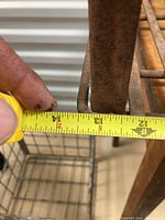 Photo showing width measurement of approx 13.5 inches of the metal crate using a tape measure.