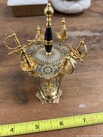 Top view showing six gold-tone sword-shaped hors d’oeuvres picks mounted on decorative holder with enamel details