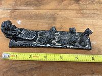 Side view of the black soapstone dogsledding carving measuring about 6 inches with a tape measure placed alongside.