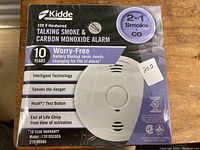 Front view of new Kidde 120V hardwired talking smoke and carbon monoxide alarm in original box showing product image and key features.