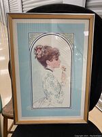 Full view of the framed watercolor artwork showing a lady in vintage dress holding a flower, with blue double matting and wooden frame.