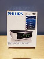 Photo of the Philips alarm clock box showing product image, branding and features including FM digital tuning, dual alarm, and battery backup.