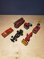 Overview of eight vintage metal toy vehicles including fire trucks, race car, and others on wooden surface.
