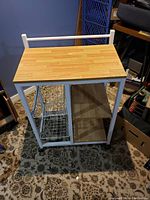 Front view of kitchen cart showing wood top surface, metal basket on left side, and two open shelves on right side.