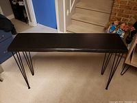 Full view of rectangular hall table with thin black metal hairpin legs and dark wood live edge top.