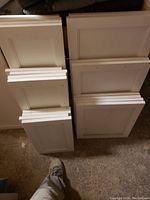 Stack of white maple shaker style cabinet doors with drilled holes and simple recessed panel design.
