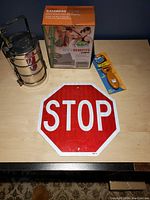 Lot contents including stop sign, tiffin lunchbox, Conair Body Benefits muscle relief pack, and pet grooming brush on a wooden surface