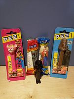 Photo showing five Pez dispensers including Pink Panther, Star Wars characters Chewbacca and Darth Vader, and one loose Darth Vader dispenser, all with original packaging and candy where applicable.