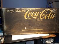 Front view of the antiqued Coca-Cola metal sign showing the text 'Enjoy/Savourez Coca-Cola' with visible wear and rust.