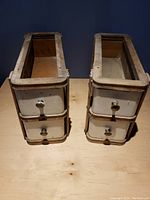 Two retro wooden sewing machine drawers with cream-colored fronts and metal knobs, showing front view of drawers open inside wooden frames.
